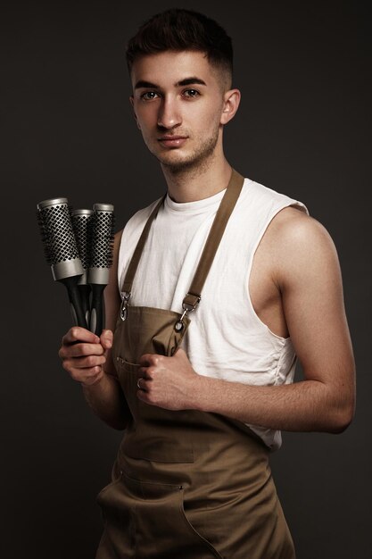 Peluquero de hombre guapo en un uniforme de trabajo con peines de cepillado en sus manos