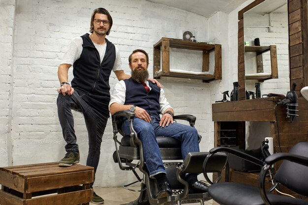 Peluquero y joven barbudo posando para la cámara antes de un corte de pelo.