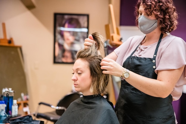 Peluquero con máscara contra la gripe teñiendo el cabello del cliente en el salón