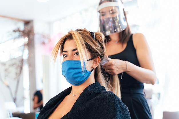 Peluquero con mascarilla planchando el cabello de un cliente