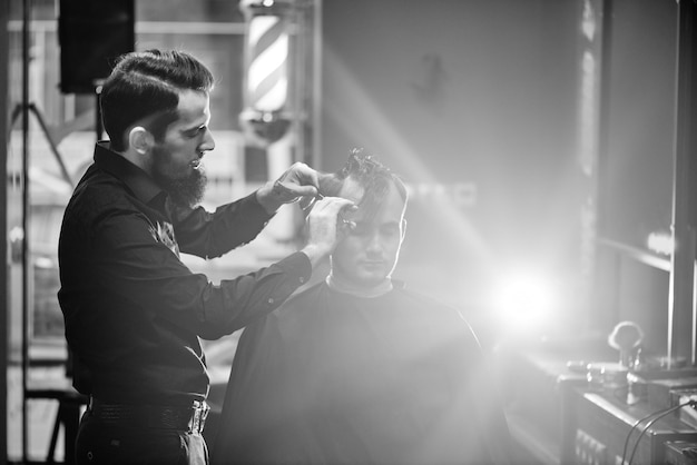 Peluquero masculino corta cliente con tijeras en la barbería Foto en blanco y negro