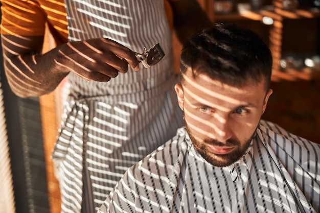 Peluquero masculino cortando el cabello del cliente con cortadora de pelo vintage