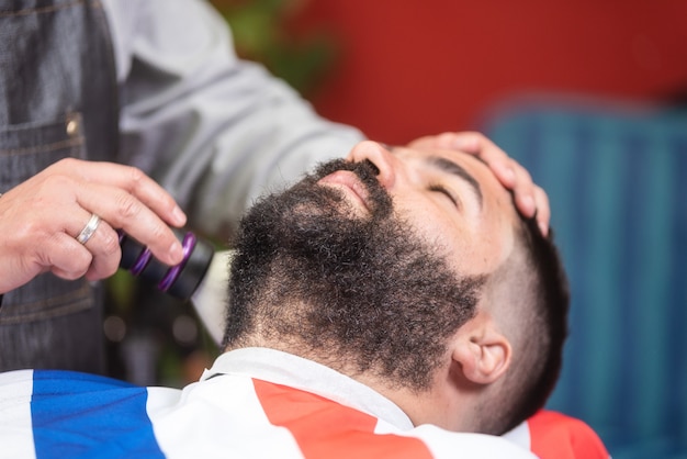 Peluquero del peluquero que limpia la barba con un cepillo en una peluquería.