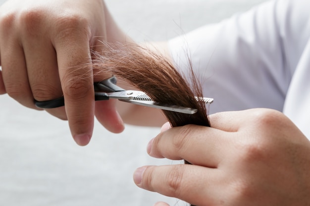 Foto peluquero del primer que arregla el pelo marrón con las tijeras.