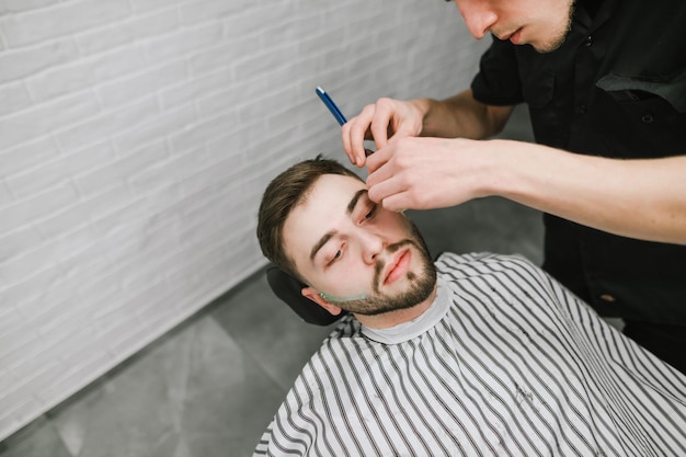 Peluquero profesional afeita a un cliente barbudo con una navaja de afeitar