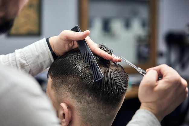 Peluquero profesional haciendo corte de pelo a hombre joven con tijeras y peine en la barbería