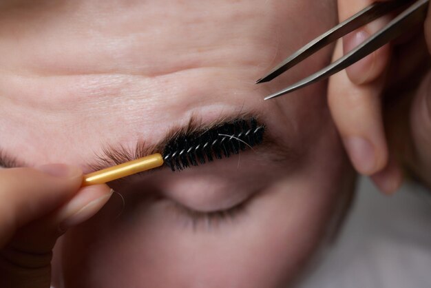 Peluquero profesional haciendo procedimiento de enhebrado y corrigiendo la forma de las cejas a un joven cliente masculino con pinzas en la peluquería Peluquería en el trabajo Concepto de cuidado de cejas Depilación de cejas