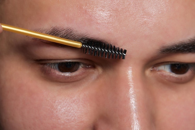 Peluquero profesional haciendo procedimiento de enhebrado y corrigiendo la forma de las cejas a un joven cliente masculino con pinzas en la peluquería Peluquería en el trabajo Concepto de cuidado de cejas Depilación de cejas