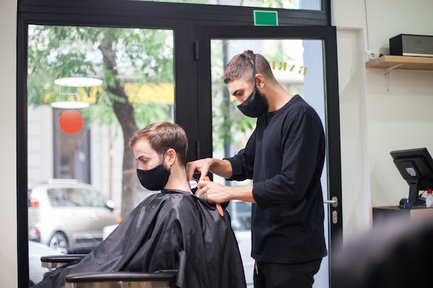 Un peluquero profesional con máscara protectora cortando el cabello a un cliente durante el coronavirus