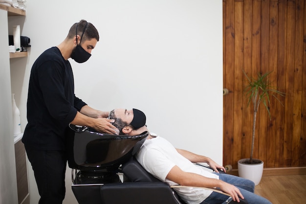 Foto un peluquero profesional con máscara protectora cortando el cabello a un cliente durante el coronavirus