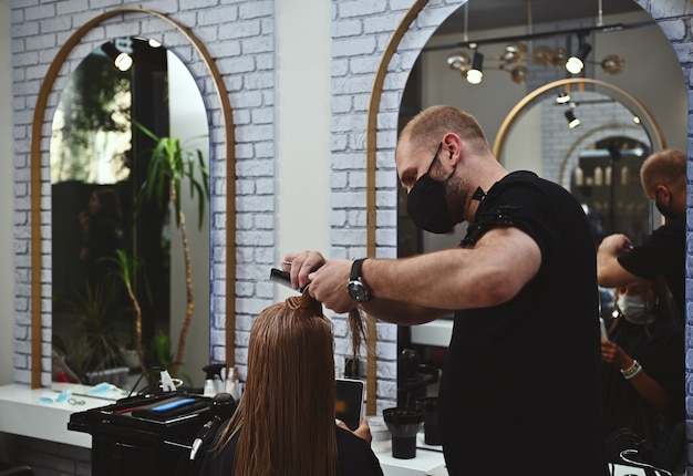 Un peluquero profesional masculino peinando y cortando el cabello largo y húmedo del cliente del salón de belleza