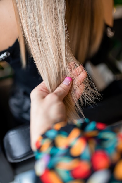 Un peluquero profesional prepara cabello rubio para extensiones en un salón de belleza mientras lo prueba para un cliente