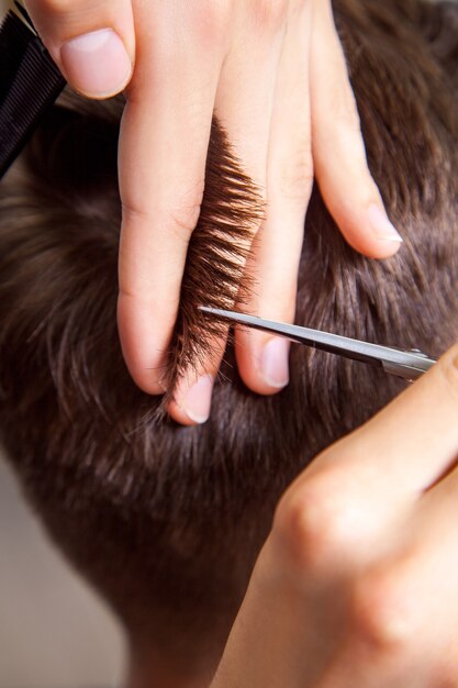 Peluquero profesional recortar joven con la ayuda de tijeras y peine.