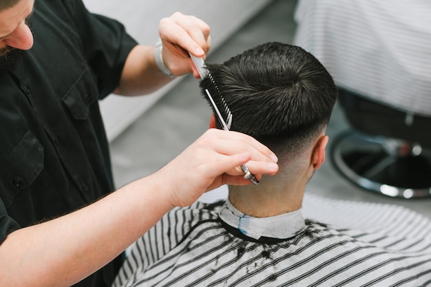 Foto el peluquero recorta a un hombre en una peluquería ligera con tijeras. concepto de corte de pelo men39s