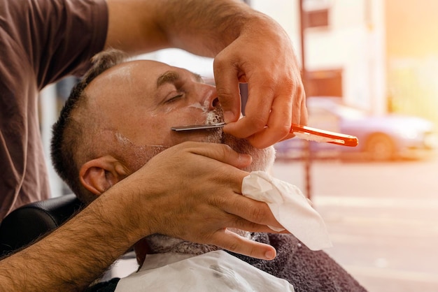 Peluquero recortando y cortando al hombre barbudo con máquina de afeitar en la barbería Proceso de peinado