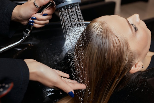 Foto el peluquero en el salón de belleza lava el cabello de su cliente antes del procedimiento de aplicación de ingredientes restauradores naturales y vitaminas para el cabello y el corte de cabello