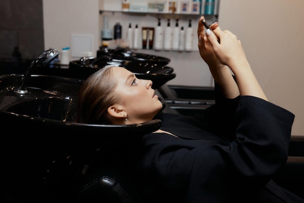 El peluquero en el salón de belleza lava el cabello de su cliente antes del procedimiento de aplicación de ingredientes restauradores naturales y vitaminas para el cabello y el corte de cabello