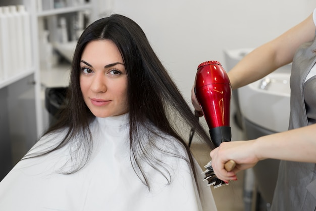 El peluquero seca el cabello mojado de las chicas con un secador de pelo y lo peina