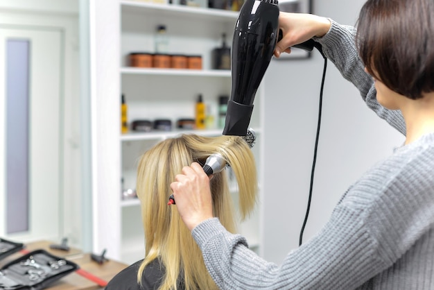 peluquero seca el cabello con un secador de pelo mujer en el salón. primer plano.concepto de belleza y moda