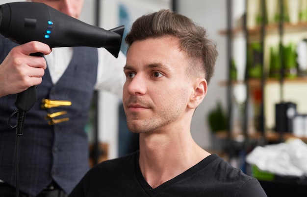 Peluquero secando el cabello de un cliente masculino en el salón