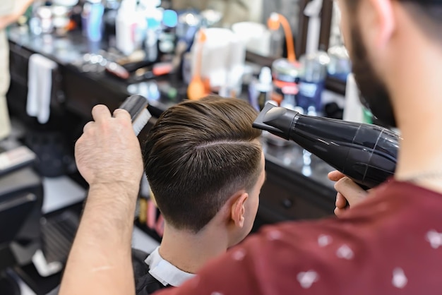 Peluquero secando el cabello de su cliente. El peluquero hace el peinado del cabello con un secador de pelo. Enfoque selectivo.