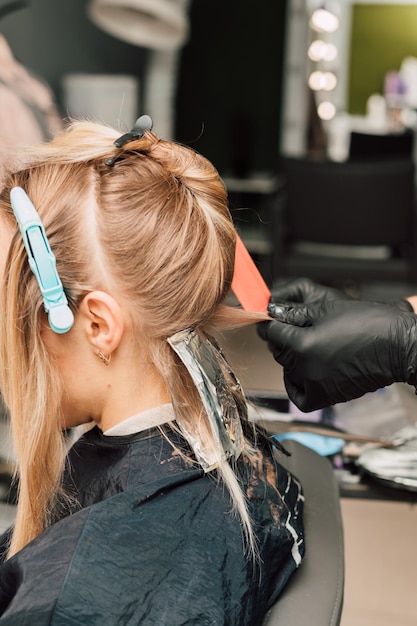 Peluquero tiñe mechones de cabello a un cliente con guantes negros