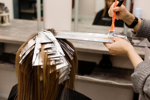 Foto el peluquero está tiñendo el cabello femenino haciendo reflejos en el cabello de su cliente con una lámina