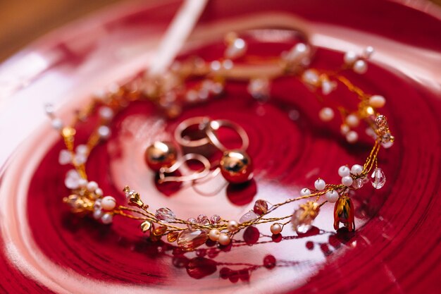 Pendientes de diamantes y anillos de boda yacen con la tiara en un plato rojo Detalles de la boda