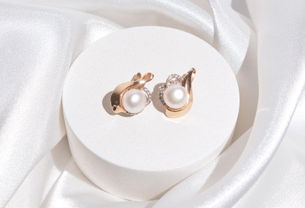 Pendientes de perlas con accesorios dorados sobre fondo de seda blanca Hermosos accesorios para mujer Regalo de joyería elegante o regalo para boda o día de San Valentín