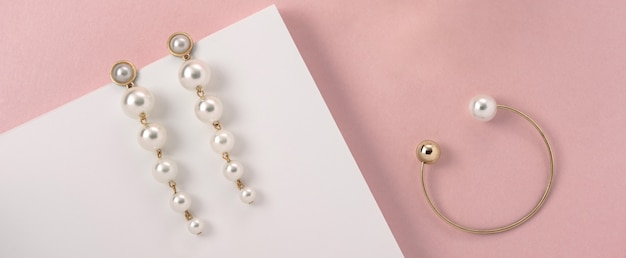 Pendientes de perlas y pulsera dorada sobre superficie rosa