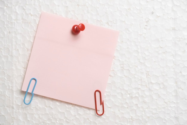 Pendurado na parede com botões de papelaria de ajuda está um adesivo rosa para anotações