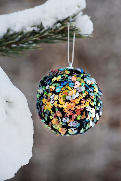 Pendurando uma bola de Natal multicolorida e brilhante em abeto e sobre fundo desfocado