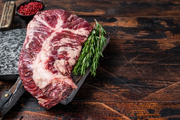 Pendurar o bife de carne crua tenro ou cabide na mesa de açougueiro com cutelo. Mesa de madeira escura. Vista do topo.