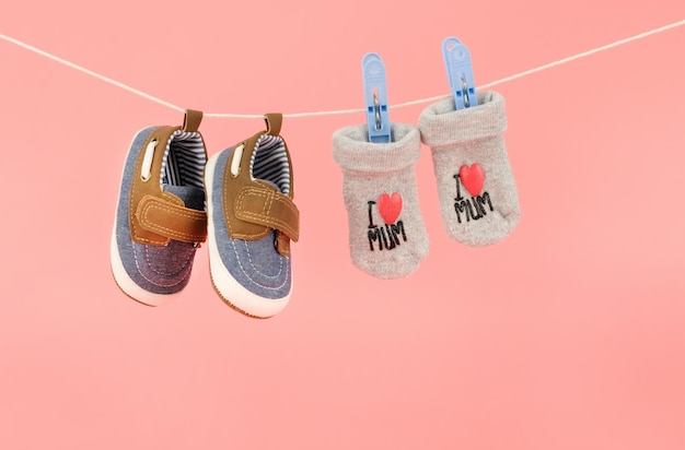 Pendurar sapatos de bebê e meias isoladas no conceito de roupas de bebê de fundo rosa