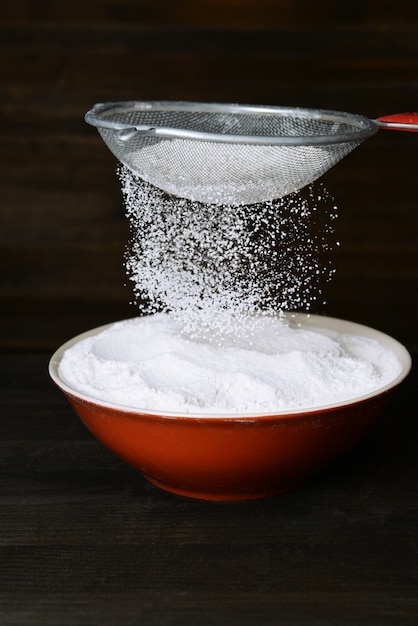 Peneirar farinha em uma tigela na mesa de madeira