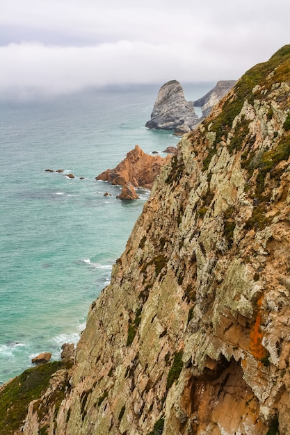 Penhascos rochosos à beira do mar Atlântico e nevoeiro ao fundo no horizonte.