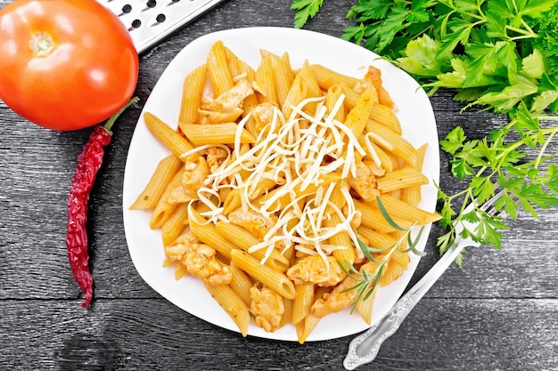 Penne com frango e tomate no prato no topo da placa escura