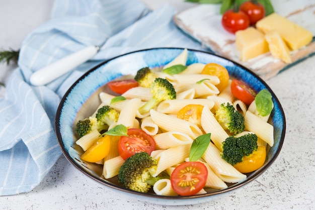 Penne cozido com legumes, brócolis, tomate e ervas frescas. Close-up, foco seletivo.