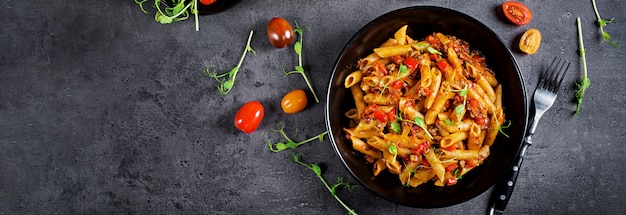 Foto penne nudeln in tomatensauce mit fleisch, tomaten mit erbsensprossen auf einem dunklen tisch dekoriert.