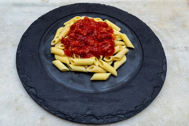 Penne-Nudeln mit in roter Soße auf einem Steinteller, Stein oder Betonhintergrund