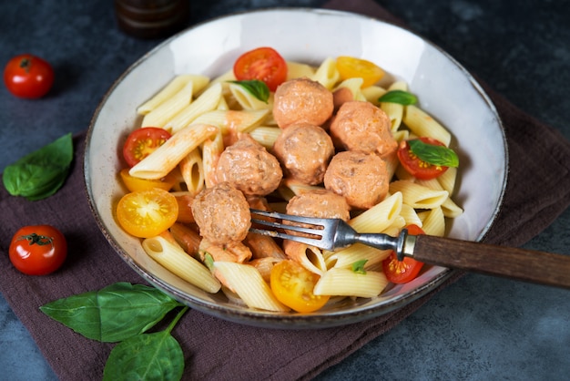 Penne pasta con albóndigas tomates y salsa sobre un fondo oscuro