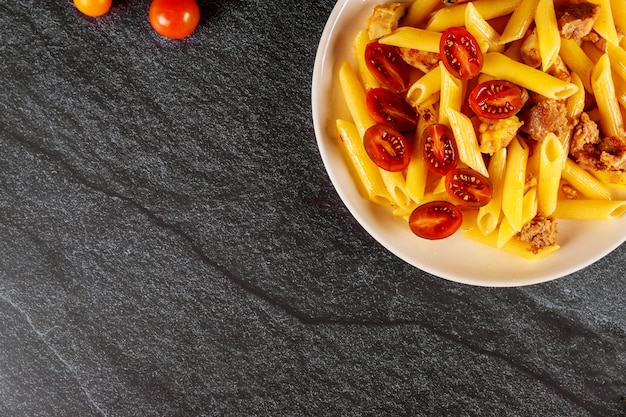 Penne pasta con carne y tomate cherry en un tazón blanco