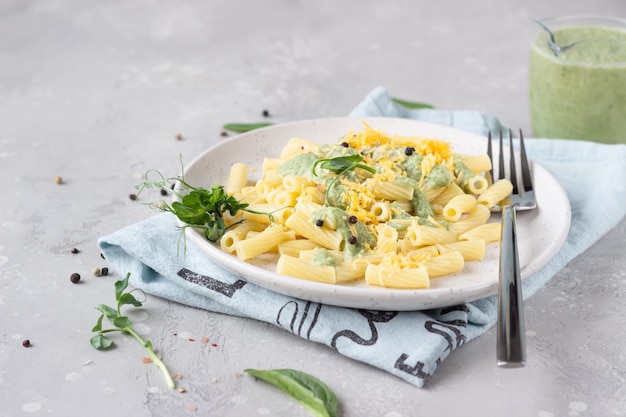 Penne Pasta mit grüner Sahnesauce, Käse und Mikrogrün auf einer Keramikplatte