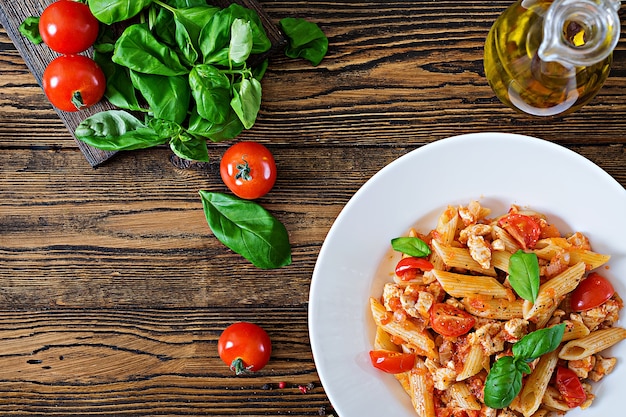 Penne pasta en salsa de tomate con pollo, tomate, decorado con albahaca