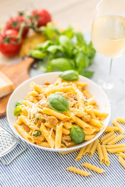 Penne de pasta con trozos de pollo, champiñones, albahaca, queso parmesano y vino blanco. Comida italiana en plato blanco sobre la mesa de la cocina.