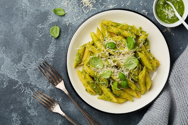 Penne Rigate Pasta mit Parmesan und Basilikumblättern in Keramikplatte auf grauem Vintage alten Betontisch.