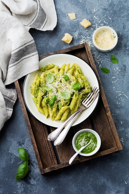 Penne Rigate Pasta mit Parmesan und Basilikumblättern in Keramikplatte auf grauem Vintage alten Betontisch.