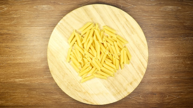 Penne Rigate Raw Pasta é uma massa curta com cortes oblíquos e uma superfície nervurada. Massa tradicional italiana. Fundo de massa. Vista superior do ingrediente alimentar italiano na mesa marrom.