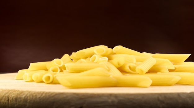 Penne rigate raw pasta ist eine kurze pasta mit schrägen schnitten und einer gerippten oberfläche. traditionelle italienische pasta. pasta-hintergrund. seitenansicht einer italienischen lebensmittelzutat auf einer holzplatte.