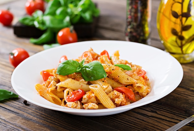 Penne-Teigwaren in der Tomatensauce mit Huhn, Tomaten, verziert mit Basilikum auf einem Holztisch. Italienisches Essen. Pasta Bolognese.